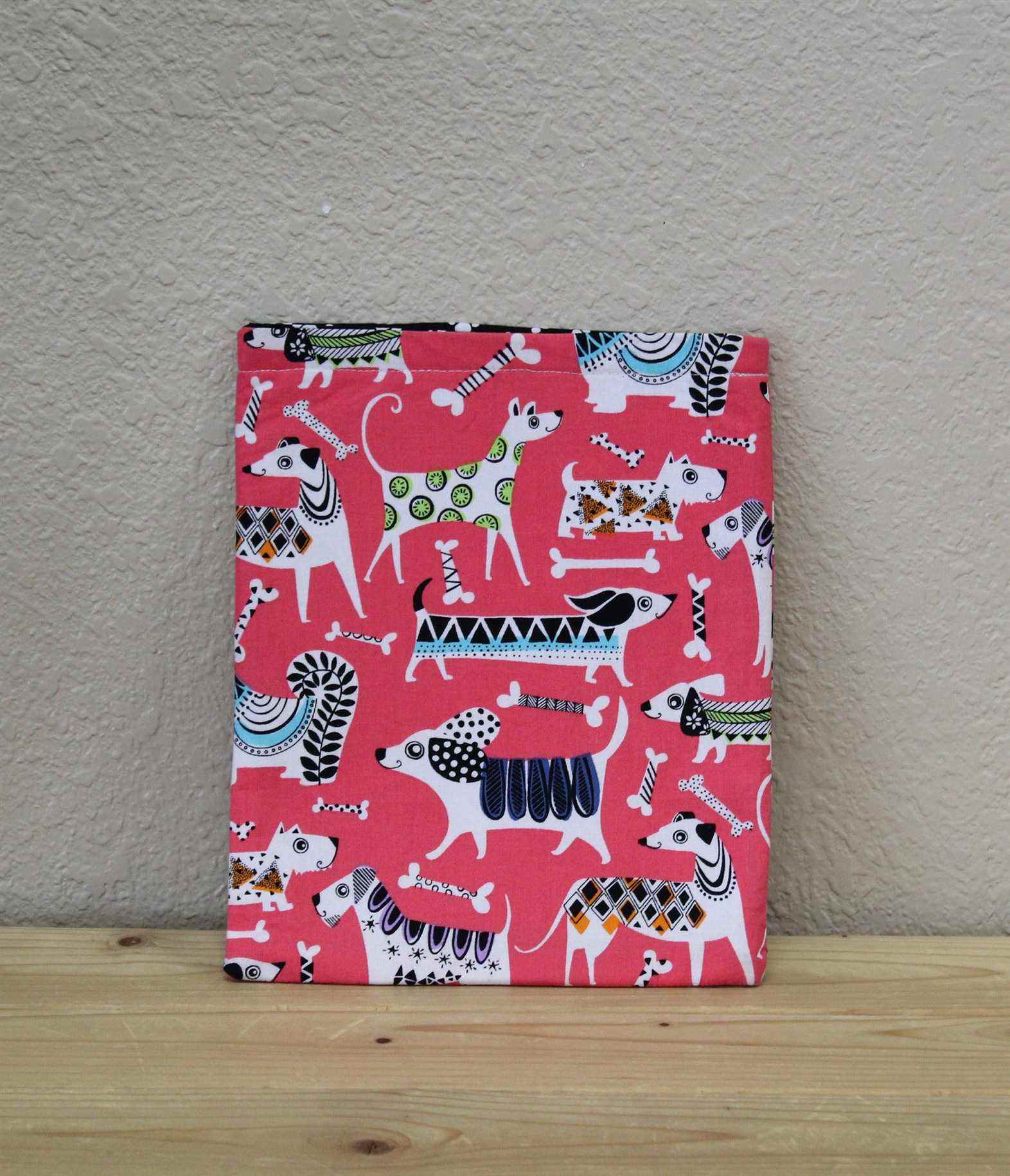 Une pochette de livre en tissu rose avec des chiens colorés dessus. 