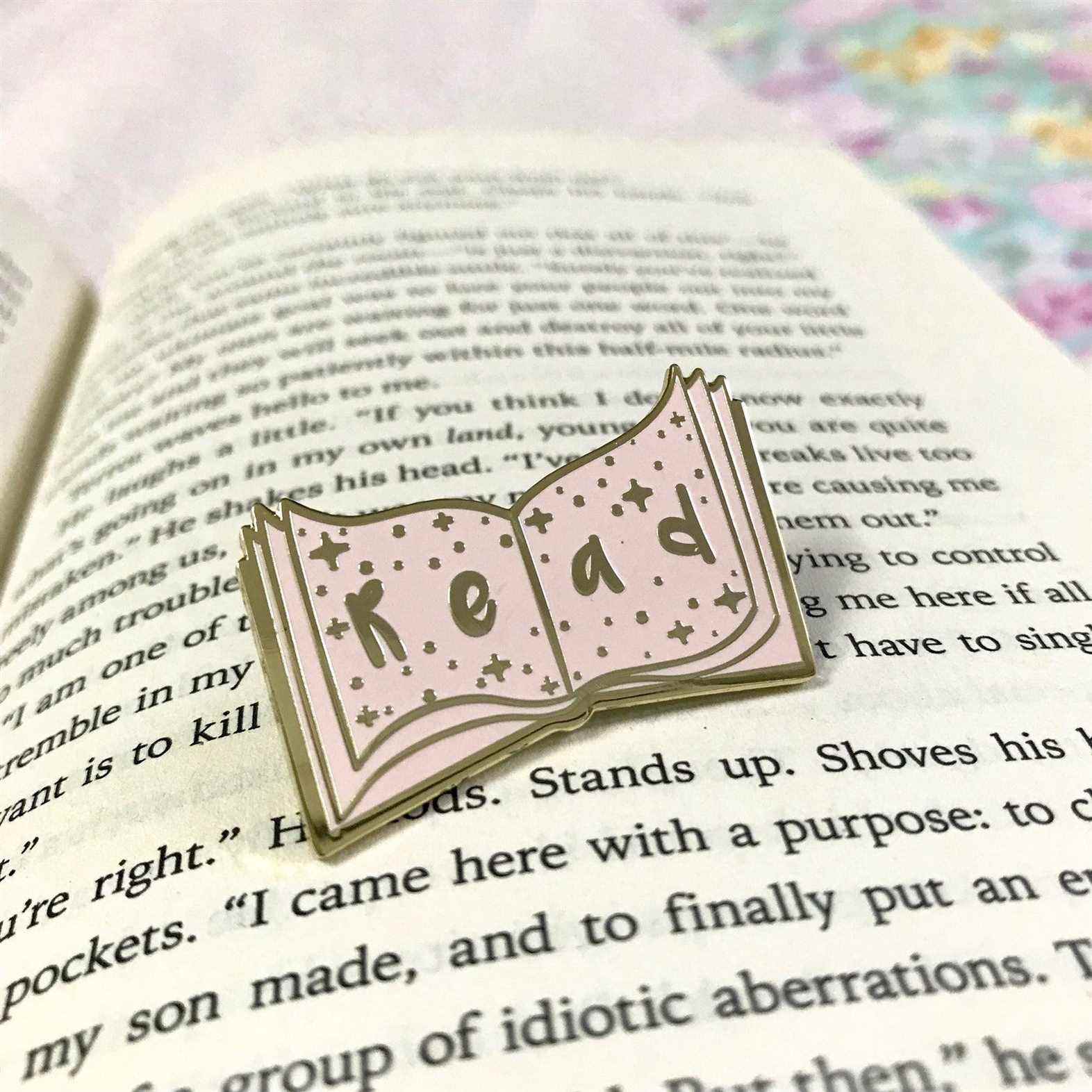 Épingle en émail rose posée sur un livre ouvert.  Ça lit 
