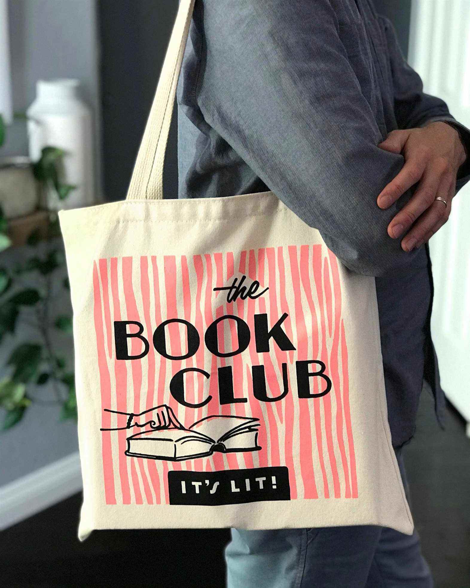 Image d'un sac fourre-tout en toile.  Il a des rayures roses et les mots "Le club de lecture : c'est allumé" en caractères noirs, avec une image d'un doigt pointant dans un livre ouvert. 