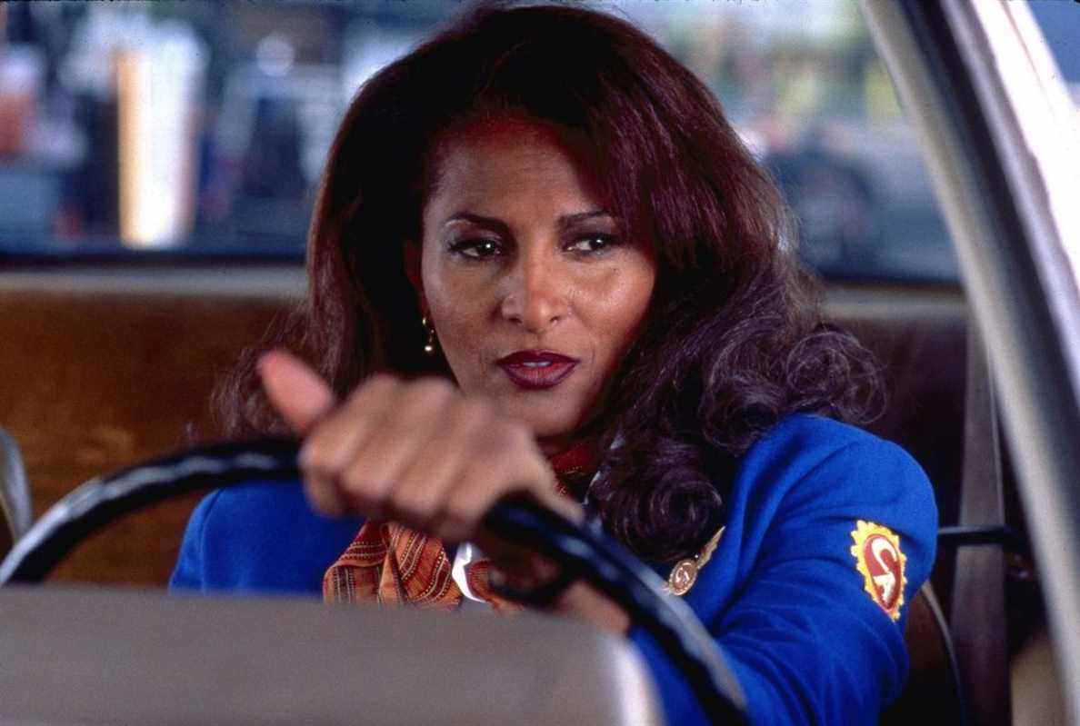 vêtue d'une veste d'hôtesse de l'air bleue, Jackie (Pam Grier) est assise au volant d'une voiture dans Jackie Brown