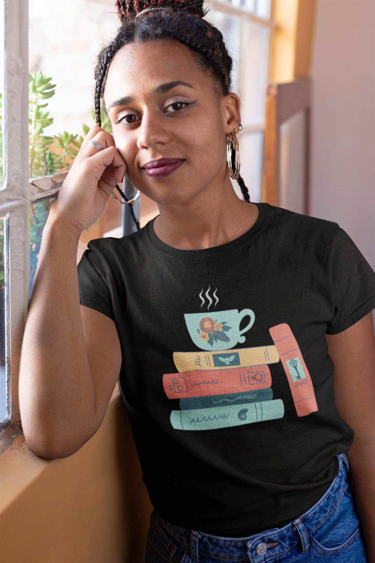 Image d'une femme noire portant un t-shirt noir.  La chemise a une tasse de thé vert au-dessus de quatre livres en jaune, orange et vert.  Il y a un cinquième livre appuyé contre la pile. 