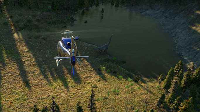 Une capture d'écran de Jurassic World Evolution 2, où un hélicoptère vole au-dessus et derrière un grand dinosaure herbivore au long cou, à côté d'un petit lac