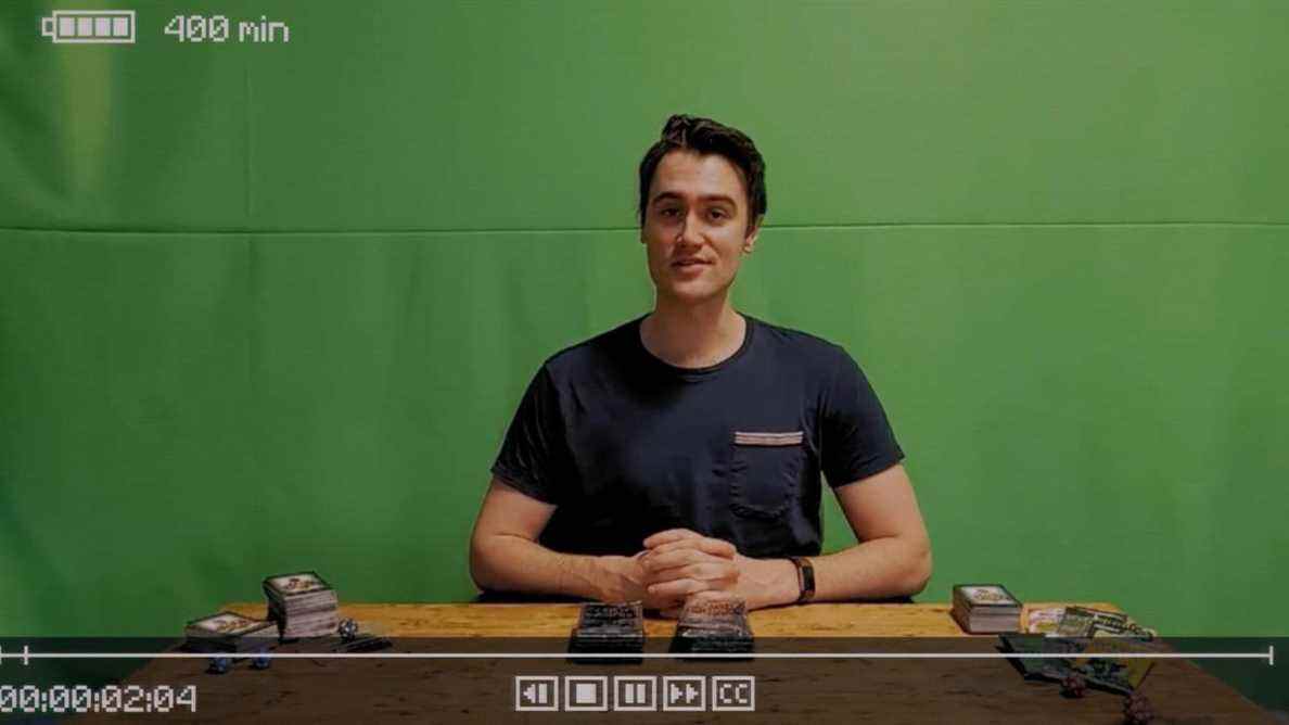 Inscryption - Luke Carder, un jeune homme devant un fond d'écran vert, s'assoit et se prépare à enregistrer une vidéo sur les jeux de cartes