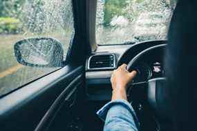 Gros plan des mains du conducteur sur le volant conduisant un jour de pluie.  (Getty Images)