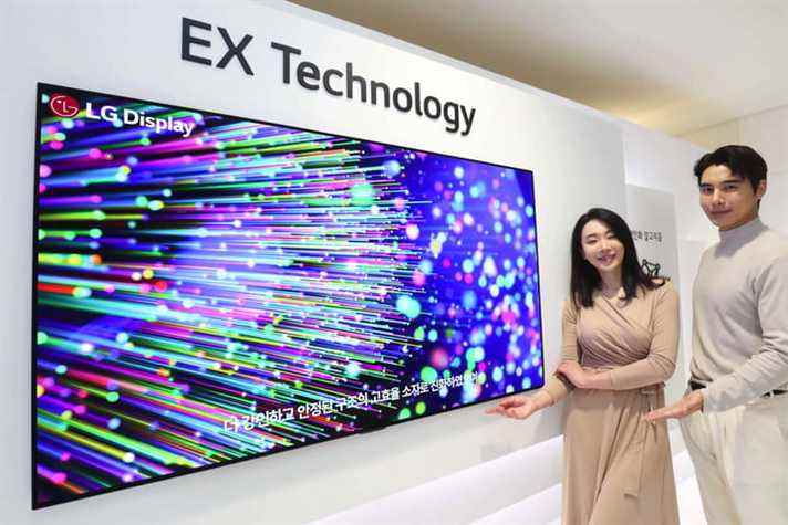 Les modèles se tiennent à côté d'une démonstration du panneau OLED EX de LG Display.