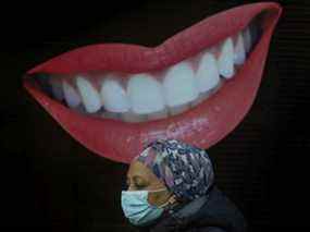 Un piéton portant un masque passe devant une bouche et des dents souriantes animées devant Dorval Dental sur la rue Bloor Ouest à Toronto pendant la pandémie de COVID 19 à Toronto, le 14 décembre 2021.