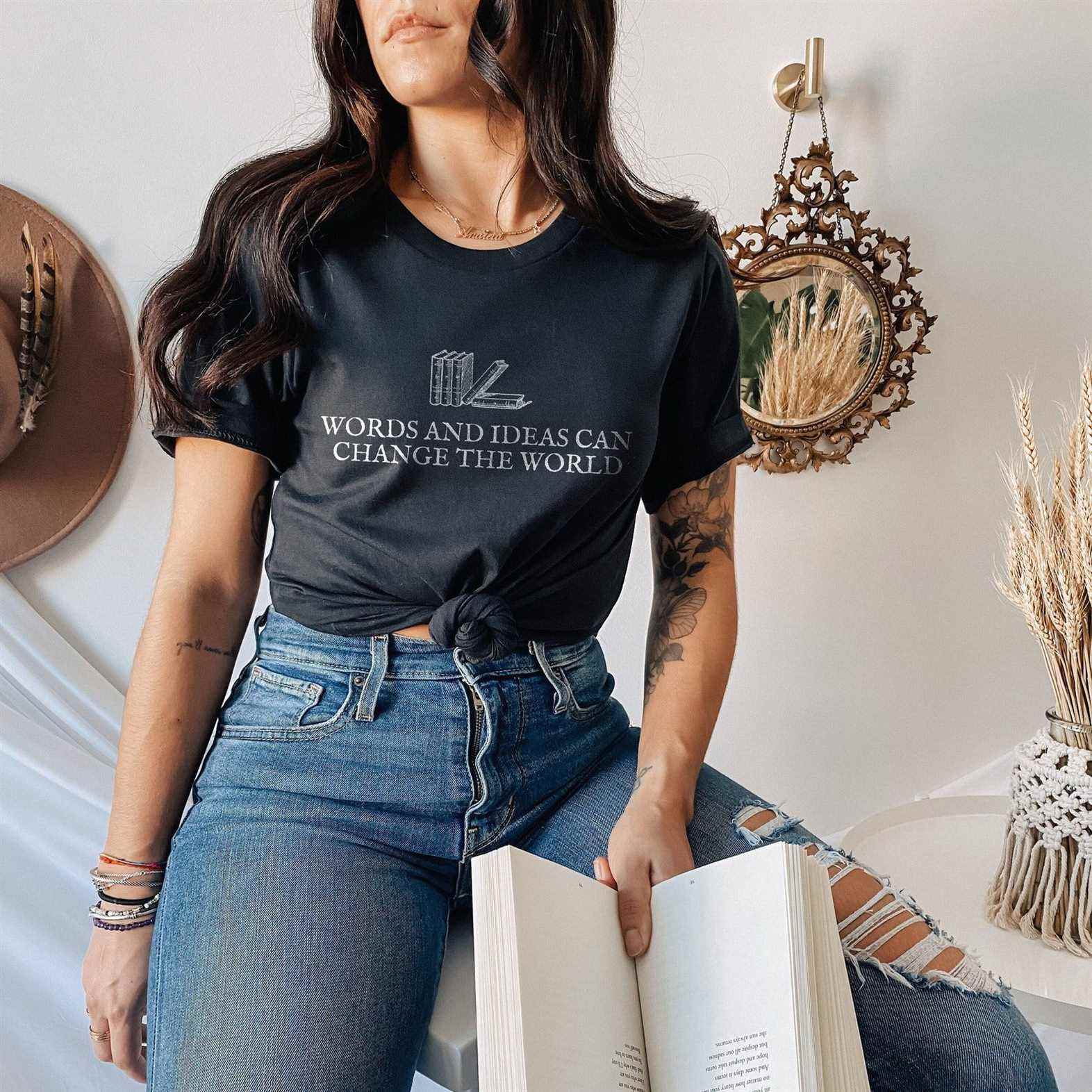 Image d'une femme portant une chemise qui lit "les mots et les idées peuvent changer le monde." La chemise est noire avec des livres dessus. 