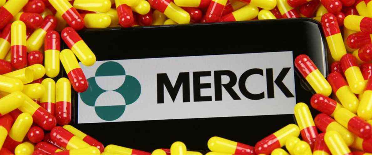 Gros plan sur l'écran du téléphone portable avec le logo de la société pharmaceutique Merck sur des capsules de médicament jaune rouge