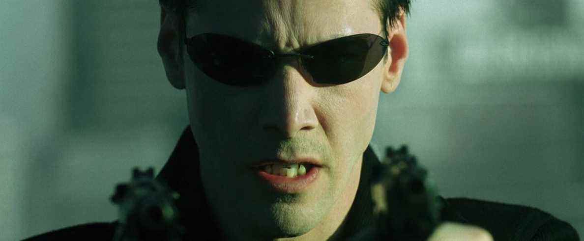 Neo tient deux pistolets tout en portant des lunettes de soleil dans The Matrix