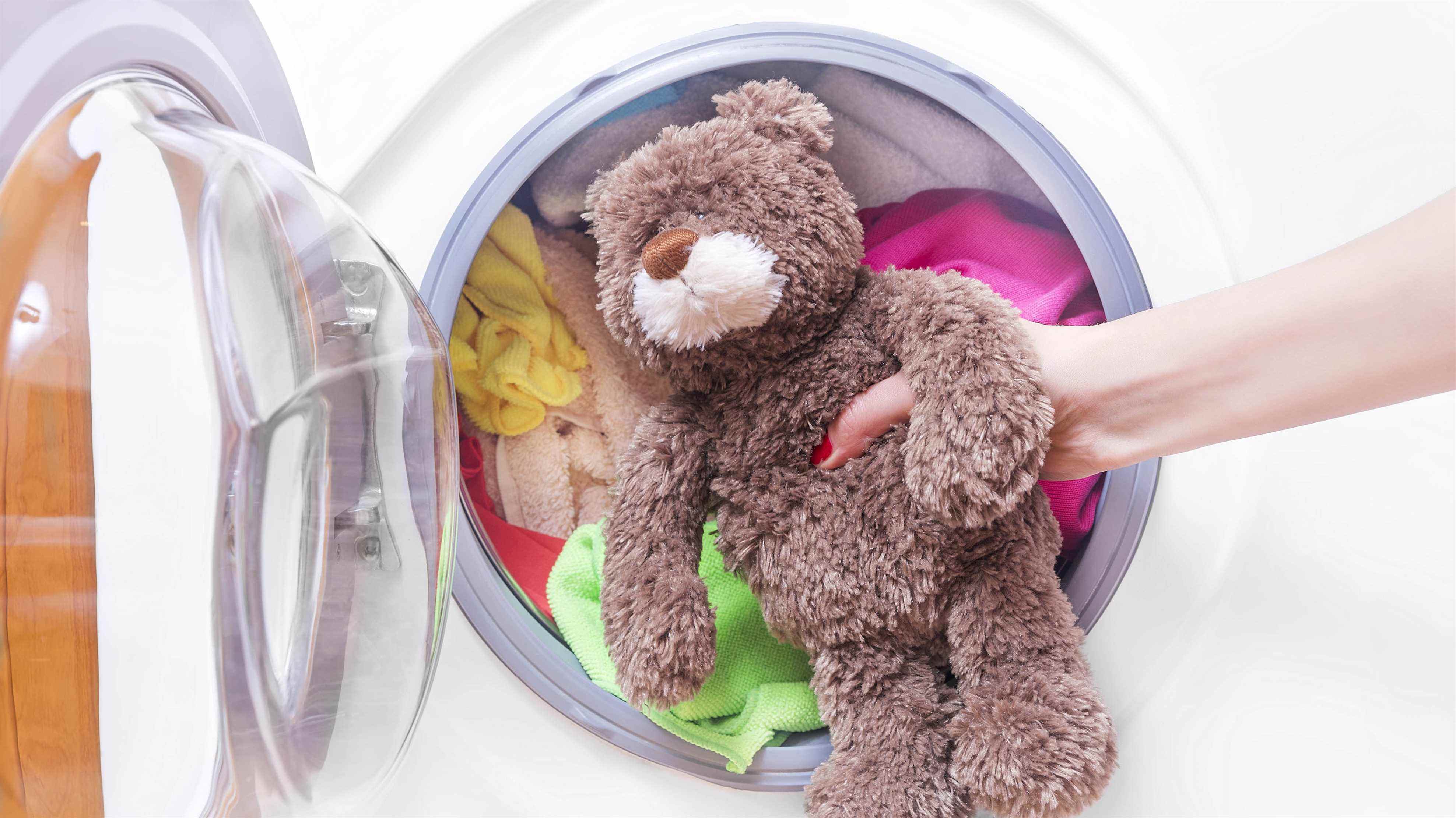 Un ours en peluche devant une machine à laver chargée