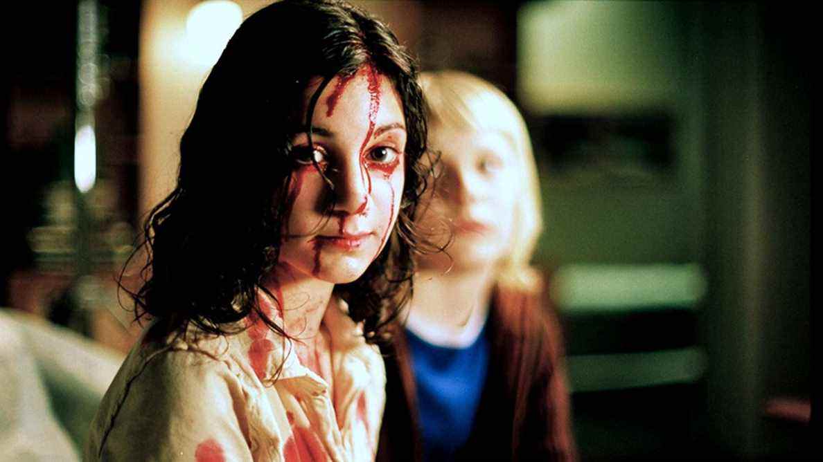 Lina Leandersson, une petite fille brune aux yeux écarquillés, est assise couverte de sang dans Let the Right One In.