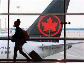 Les voyageurs se déplacent entre les portes avec un avion d'Air Canada en arrière-plan à l'aéroport international de Calgary le mardi 18 janvier 2022.