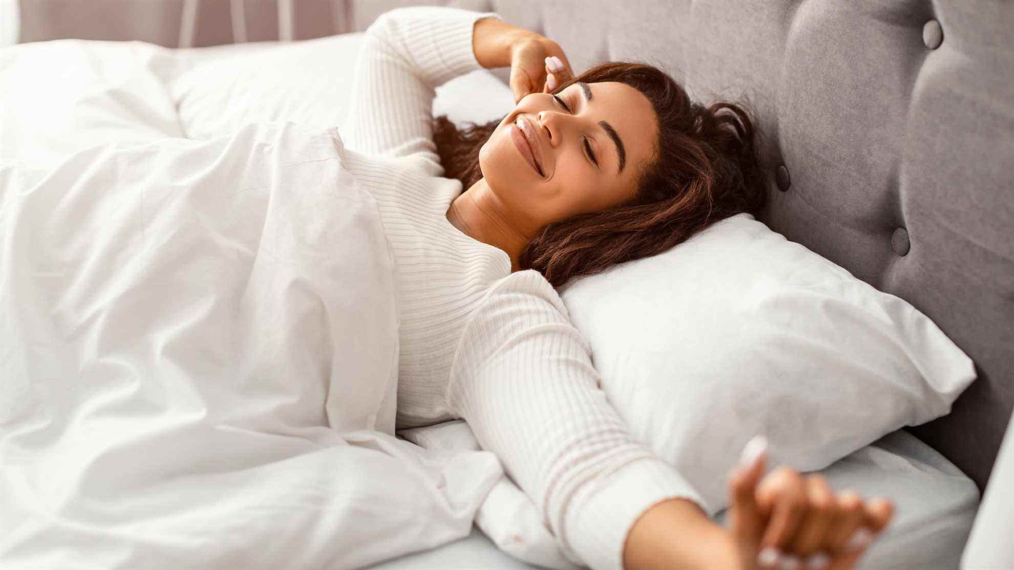 Une femme sourit et s'étire dans son lit après une bonne nuit de sommeil