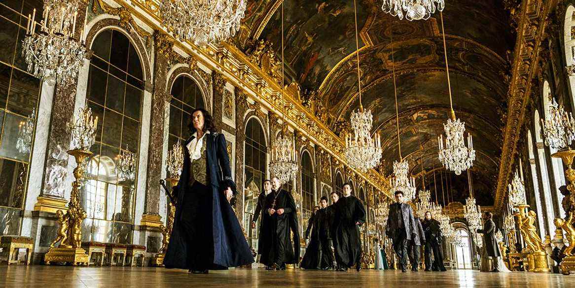 Pierce Brosnan tandis que Louis XIV traverse Versailles, entouré de dorures et de lustres