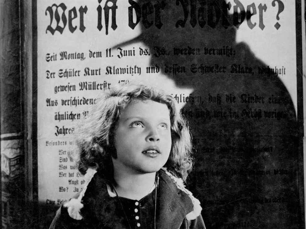 Inge Landgut dans le rôle d'Elsie Beckmann scrutant un homme se découpant sur une affiche recherchée dans M.