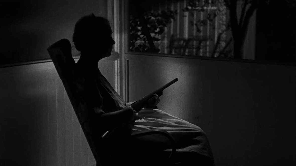 Lillian Gish dans le rôle de Rachel Cooper attendant dans un fauteuil à bascule tenant un fusil dans La nuit du chasseur.