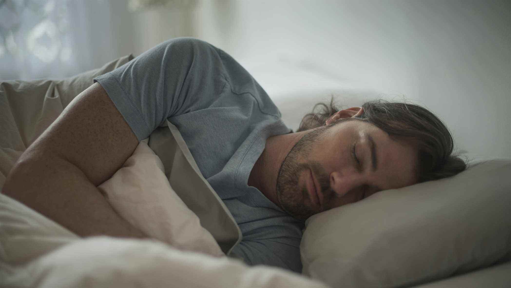 Un homme aux longs cheveux noirs dort sur le côté dans son lit
