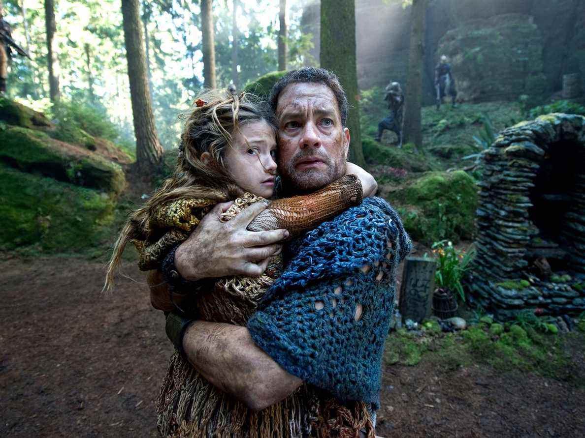 Zachry (Tom Hanks) tenant un enfant contre lui alors qu'il est entouré de maraudeurs dans Cloud Atlas.