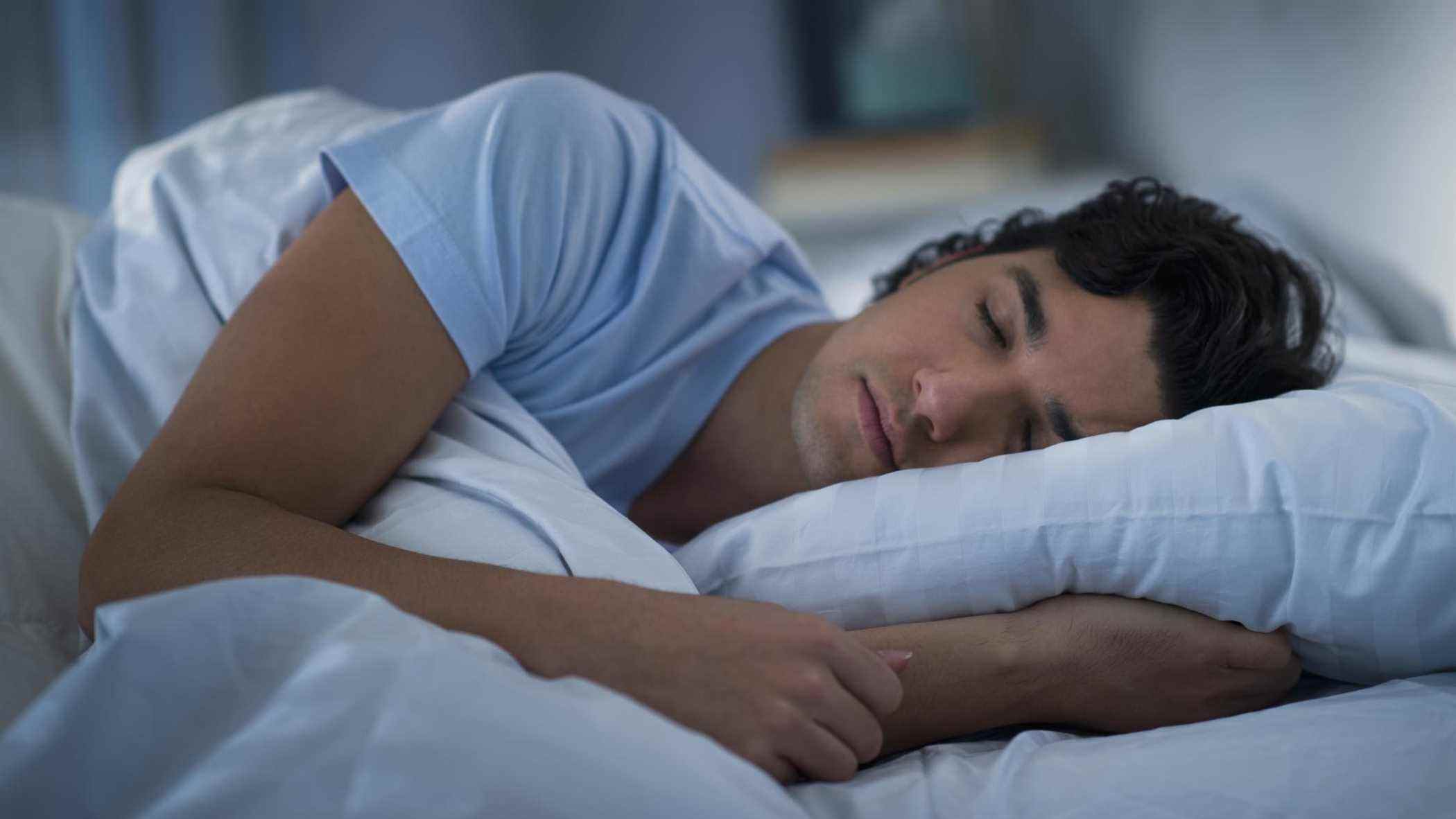 Un homme en t-shirt bleu dort sur un oreiller rafraîchissant