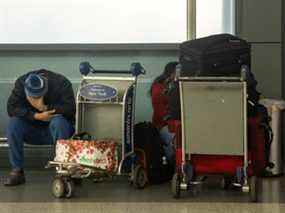 Un passager est assis avec des bagages à l'aéroport international John F. Kennedy lors de la propagation de la variante du coronavirus Omicron dans le Queens, New York, le 26 décembre 2021.