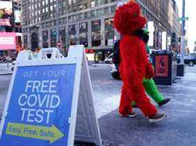 Des mascottes passent devant un panneau de test alors que les gens font la queue pour les tests Covid-19 à Times Square le 4 janvier 2022, à New York.