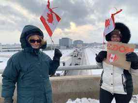 Les partisans du Freedom Convoy Fran Boudrie (L) et Mary Fenwick (R) tiennent des drapeaux canadiens tout en se tenant sur une autoroute.  Viaduc 401 à Mississauga Rd.