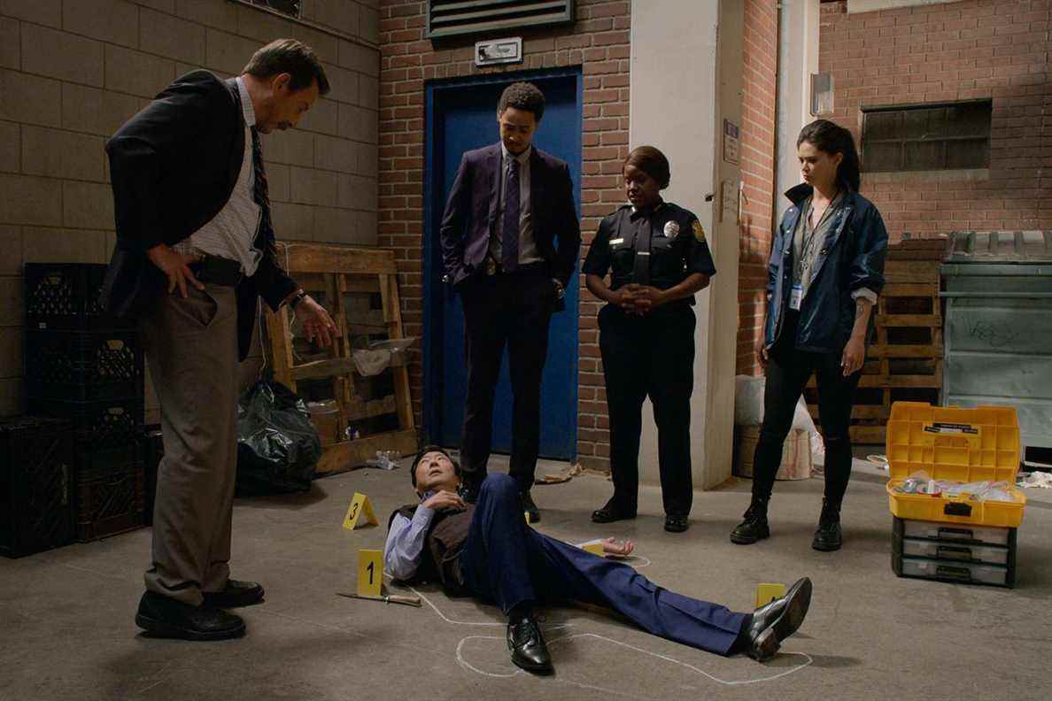 Ken Jeong allongé à la place d'un corps tandis qu'un groupe de détectives se tient autour de lui recréant la scène du crime de la finale de la saison 1 de Murderville