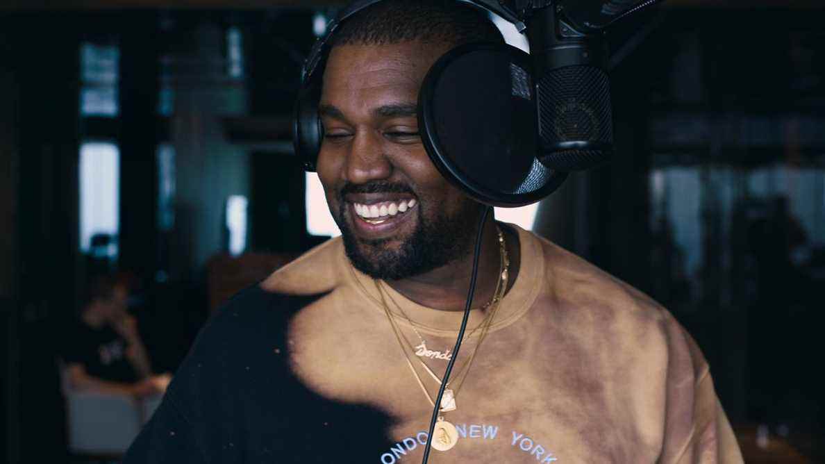 une image du troisième épisode de jeen-yuhs: A Kanye Trilogy d'un Kanye West portant un casque souriant dans un studio d'enregistrement, avec un microphone et un filtre anti-pop devant son visage