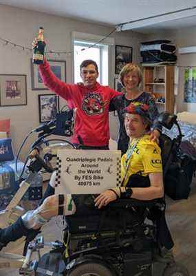 Stewart Midwinter pose pour une photo après avoir parcouru 40 075 km sur son cycle FES.  Il a célébré avec Jorge Errasquin, son assistant en physiothérapie, et Julie Muller, son épouse, coach et motivatrice.