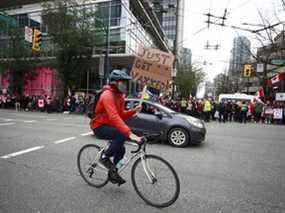 Un cycliste tient une pancarte de protestation alors qu'il descend la rue Burrard alors que des milliers de personnes se sont rassemblées au centre-ville lors d'une manifestation COVID à Vancouver le 5 février 2022.