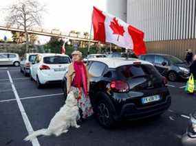 Une femme et son chien se tiennent près d'un drapeau canadien avant le début de leur « Convoi de la liberté » à Nice, en France.