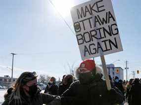 Une personne tient une pancarte alors que les gens participent à une contre-manifestation bloquant un petit convoi de camionneurs protestant contre les mandats de vaccination contre la maladie à coronavirus (COVID-19), dans la périphérie d'Ottawa, en Ontario, Canada, le 13 février 2022