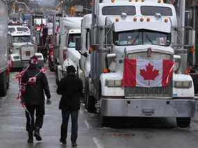 Des manifestants marchent entre des camions stationnés au centre-ville d'Ottawa alors que l'occupation du « Freedom Convoy » protestant contre les mandats de vaccination et d'autres mesures COVID se poursuit le 10 février 2022.