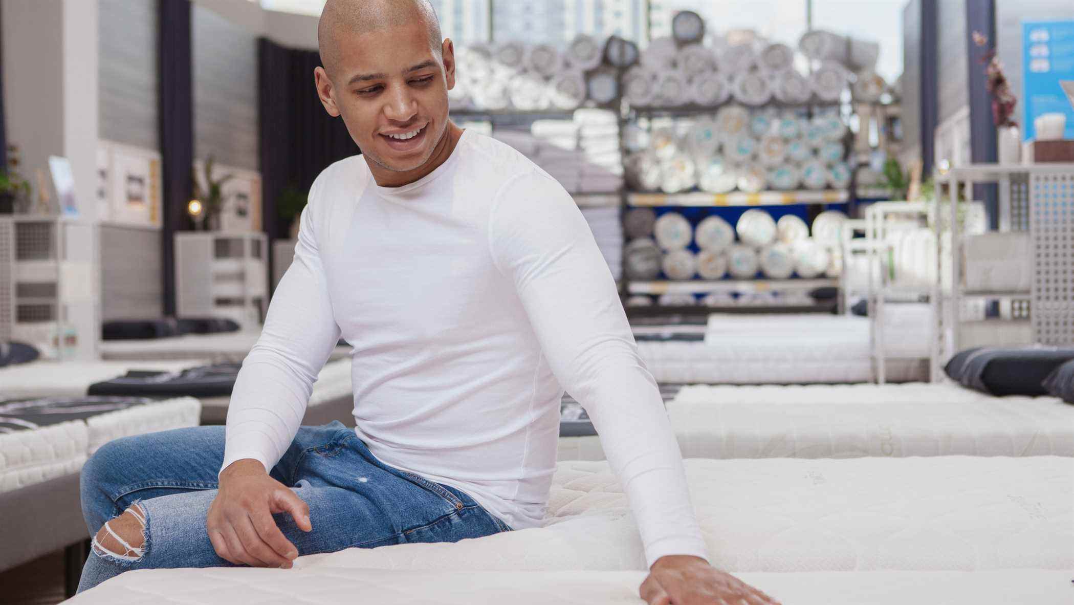 Un homme en t-shirt blanc à manches longues pose sa main sur un matelas