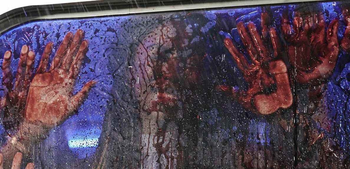Un visage ensanglanté et quatre mains ensanglantées se pressent contre l'intérieur d'une vitre de voiture incroyablement sanglante lors du massacre à la tronçonneuse au Texas en 2022