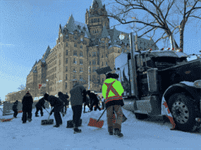 Des manifestants à Ottawa, dont au moins un enfant, pellettent de la neige pour former une barrière autour d'un camion, le 18 février 2022.