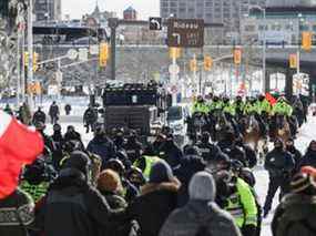 Une ligne de policiers appuyée par une unité montée et un véhicule blindé lourd avance sur des manifestants à Ottawa, le 18 février 2022.