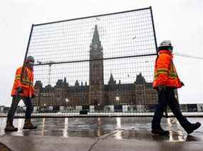 Des travailleurs transportent un morceau de clôture pour consolider les barricades existantes sur la Colline du Parlement, le 17 février 2022.