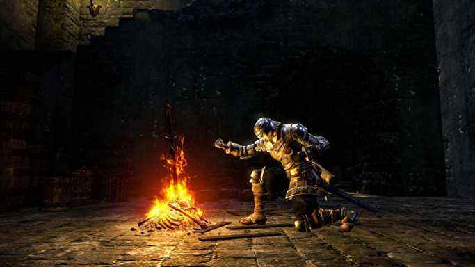 Le personnage du joueur dans Dark Souls, un chevalier vêtu d'une armure, s'agenouille devant un feu de joie