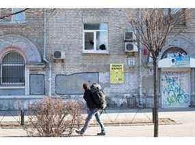 Un homme passe devant une maison avec une fenêtre brisée dans le quartier de Solomianska le 26 février 2022 à Kiev.