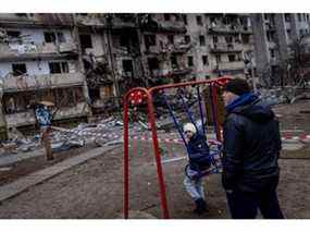Un garçon joue sur une balançoire devant un immeuble résidentiel endommagé touché par une frappe de missile tôt le matin le 25 février 2022 à Kiev.