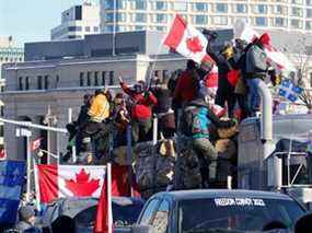 Des manifestants se tiennent sur une remorque transportant des bûches alors que des camionneurs et des partisans participent à un convoi pour protester contre les mandats de vaccination contre la maladie à coronavirus (COVID-19) pour les camionneurs transfrontaliers à Ottawa, Ontario, Canada, le 29 janvier 2022.