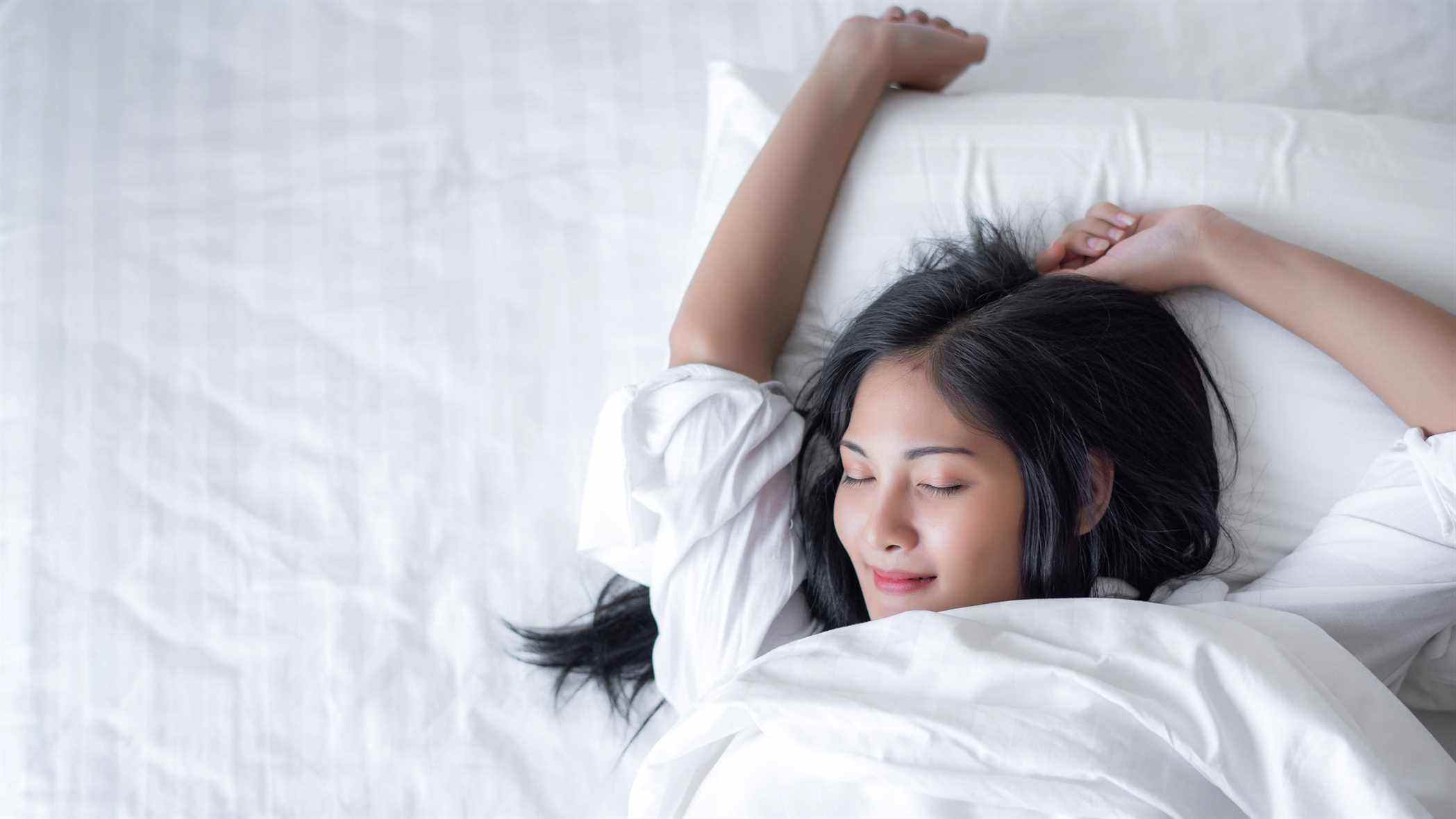 Une femme dort heureuse avec son bras levé sur un confortable matelas blanc