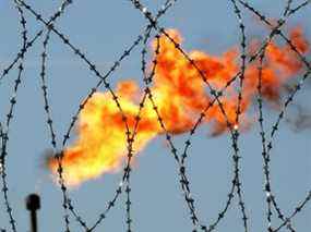 Une flamme de gaz derrière un fil de fer barbelé dans une usine de production de pétrole en Russie.