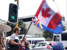 Un manifestant se tient debout avec des drapeaux néo-zélandais et canadiens près du bâtiment du parlement à Wellington le 8 février 2022, lors d'une manifestation contre les restrictions COVID, inspirée d'une manifestation similaire au Canada.