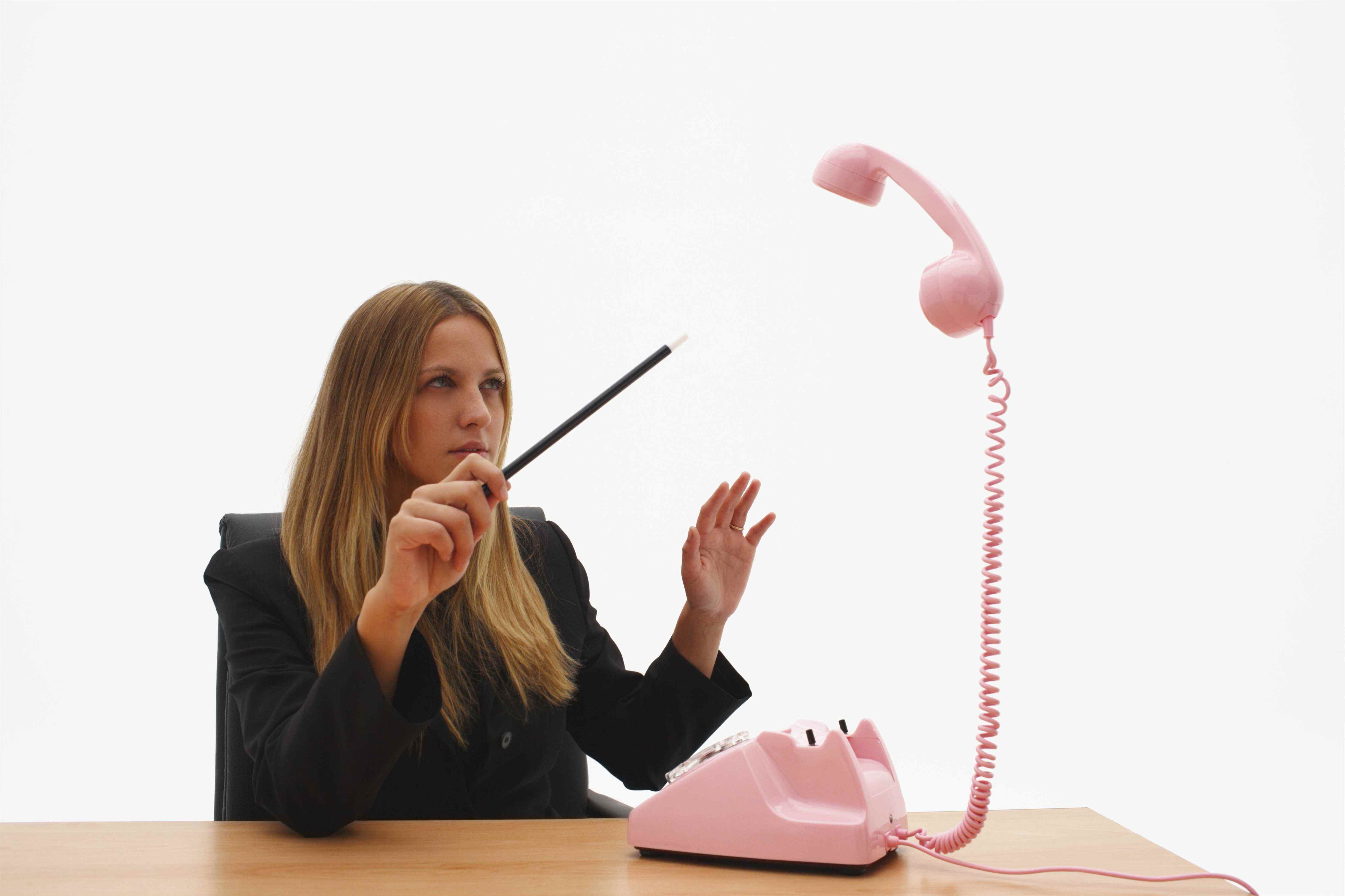 Image d'une jeune femme d'affaires pointant la baguette magique d'un magicien sur un récepteur téléphonique en lévitation.