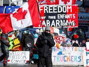 Un manifestant agite un drapeau canadien devant des banderoles en soutien aux camionneurs à Ottawa lundi.