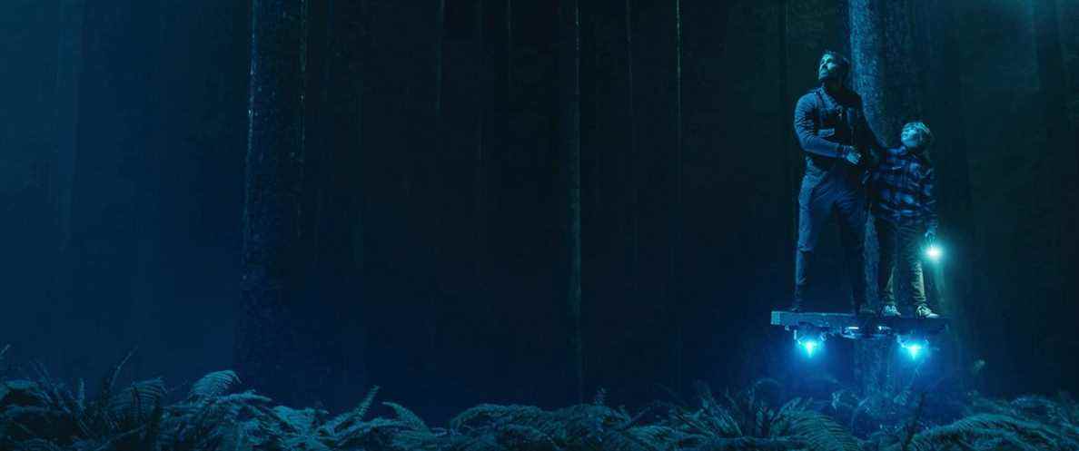 Young Adam et Big Adam (Ryan Reynolds) naviguent dans une forêt bleu foncé sur une plate-forme volante lumineuse dans The Adam Project