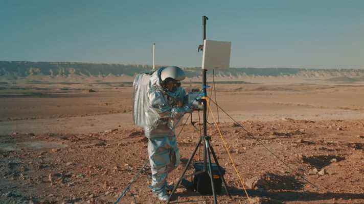 Un scientifique en costume d'astronaute ajuste certains équipements de recherche dans le désert.