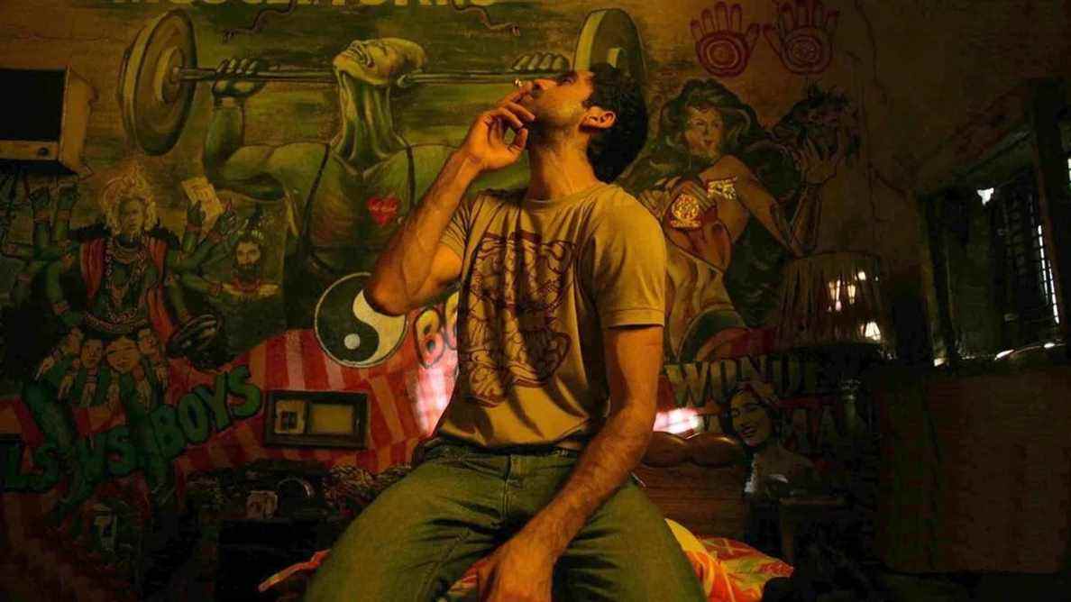 Dev (Abhay Deol) fumant une cigarette dans une pièce remplie de graffitis dans Dev.D.